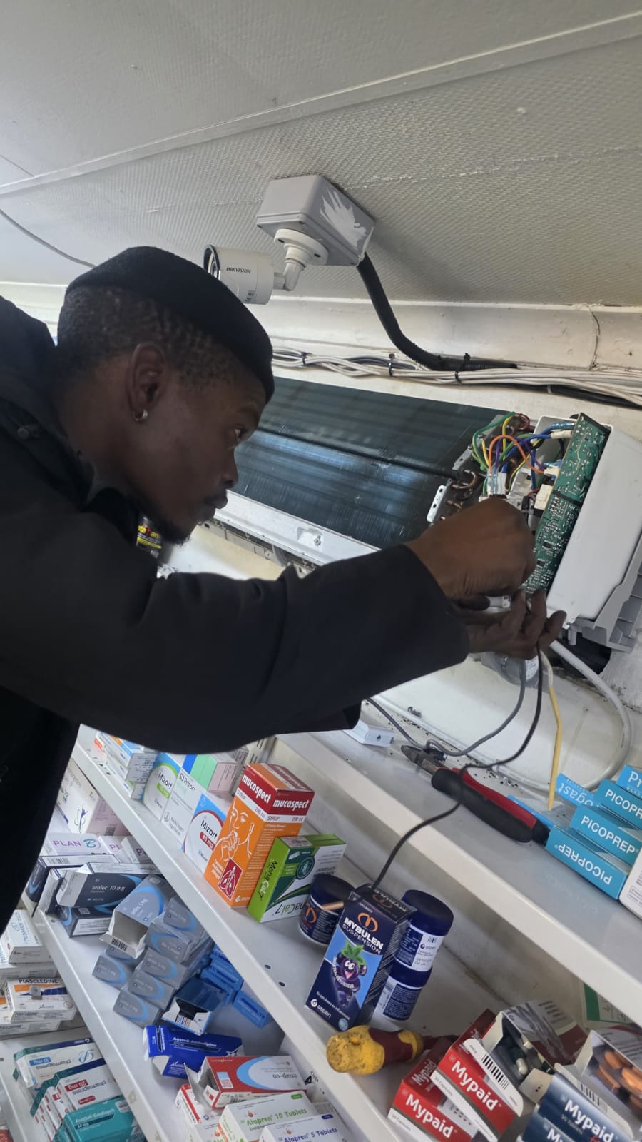 NOVA Cool technician servicing the control board of a split-system air-conditioner in a pharmacy