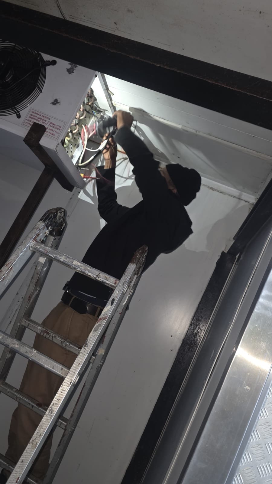 NOVA Cool technician working on cold room evaporator wiring from a ladder