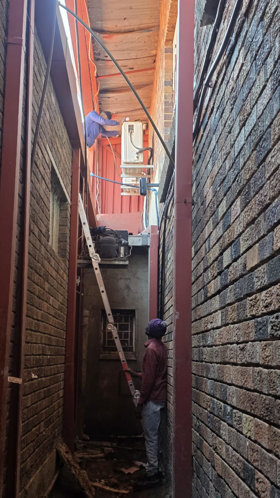 NOVA Cool team installing an air-conditioning unit in a narrow service alley